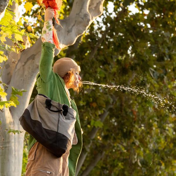 © Nuria Boleda L'artiste clown est accrochée en l'air à une branche d'arbre. Elle crache de l'eau.