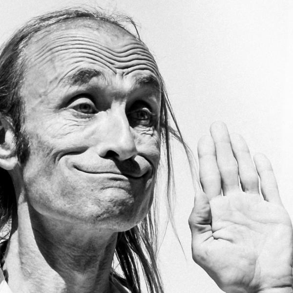 © Fanchon Bilbille Photo en noir et blanc de Patrick de Valette, sur fond blanc. Il fait une grimace en haussant les sourcils, les mains levées.