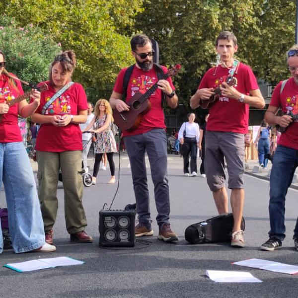 © Le C.U.T.E. Neuf musiciens et musiciennes du groupe avec leurs instruments, dans une rue de Ramonville lors du Festival de rue