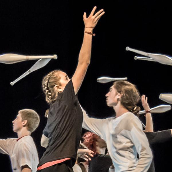 © XilloK Des jeunes marchent dans tous les sens sur scène en jonglant avec des massues.