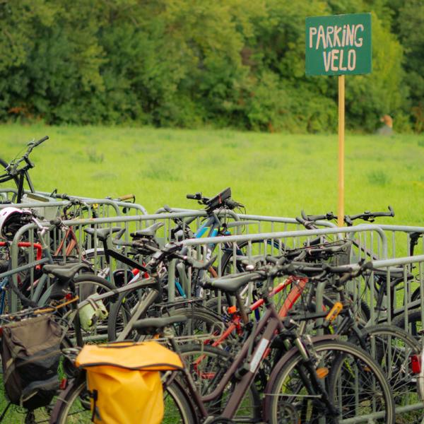 © Solveig Augereau Dans un champ, des vélos sont parqués, attachés à des barrières vauban. Une pancarte en bois colorée indique "PARKING VELO".